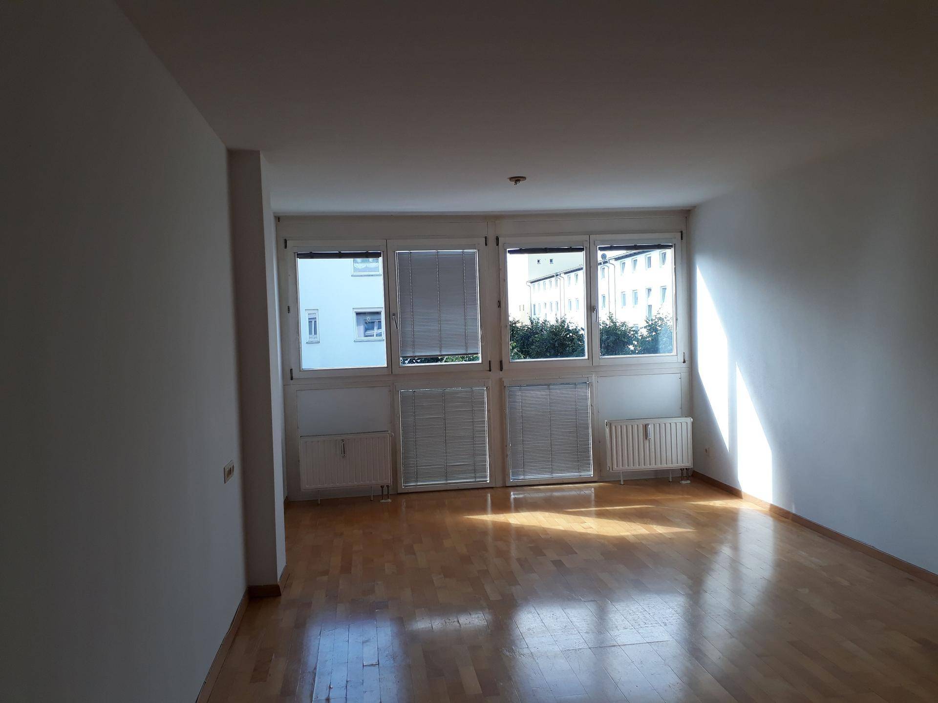 Lichtdurchflutetes Wohnzimmer mit Parkettboden und großen Fenstern zur Umgebung.
