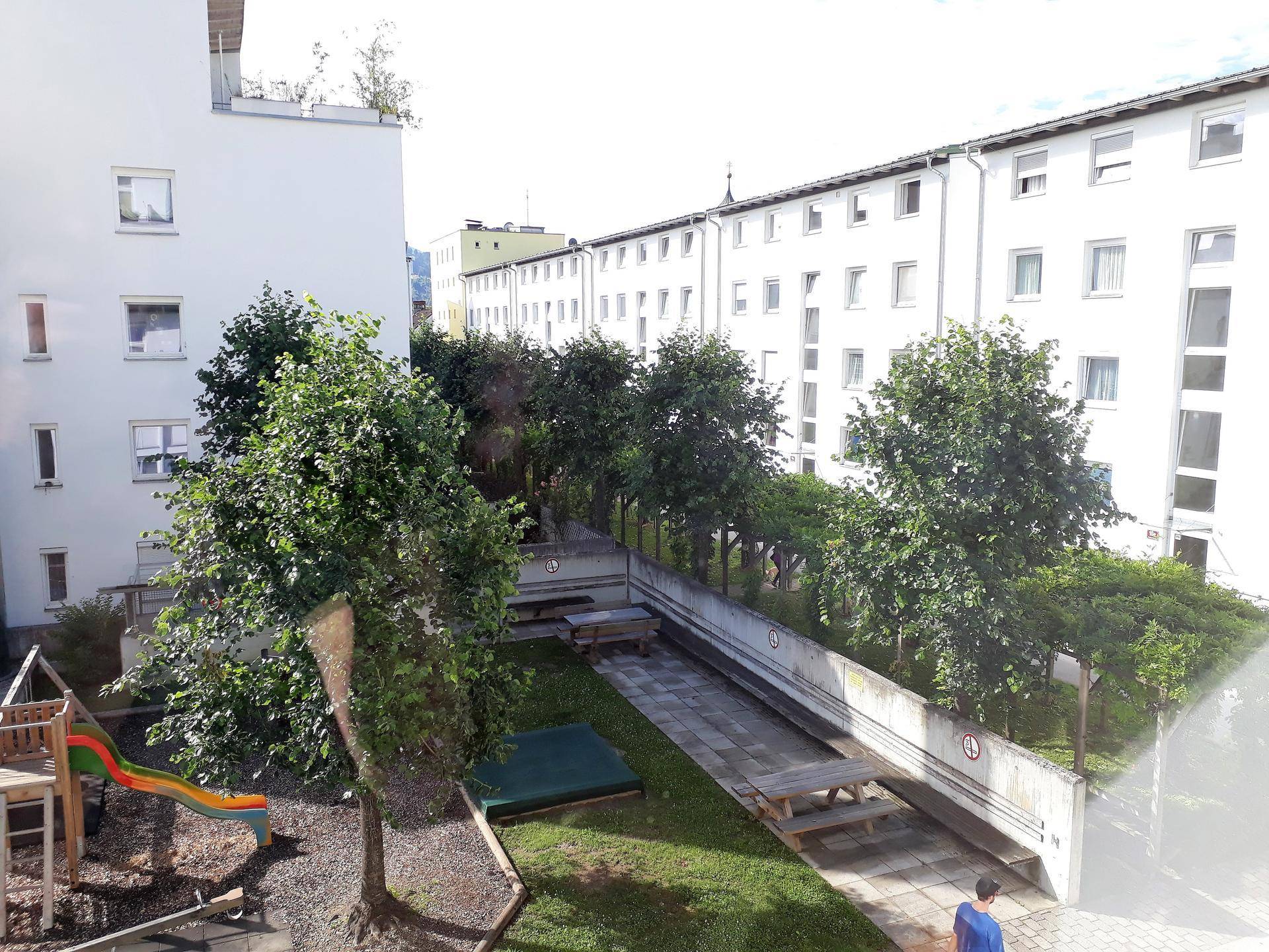 Gepflegter grüner Innenhof mit Spielplatz, Bäumen und Sitzgelegenheiten zwischen Gebäuden.