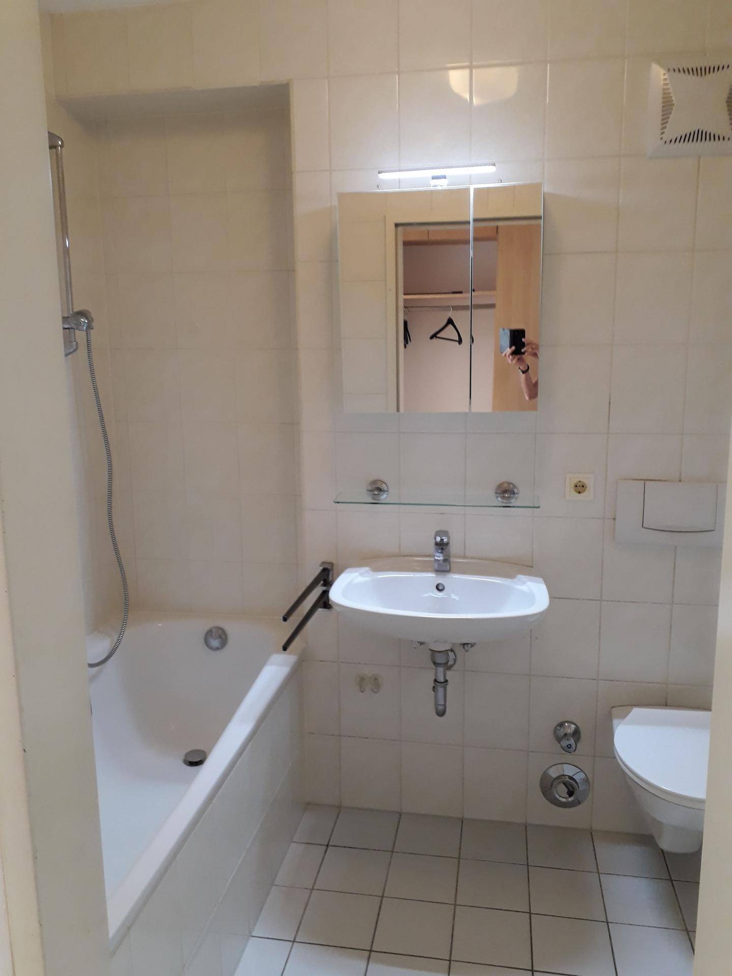 Funktionales Badezimmer mit Badewanne, Duschfunktion, Waschbecken und Spiegelschrank.