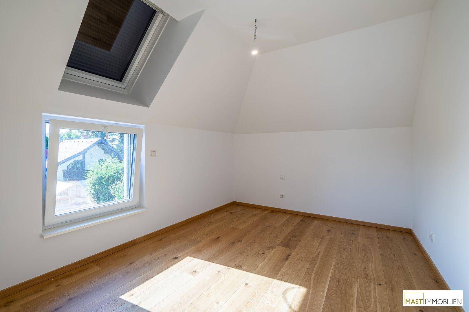 Gemütliches Zimmer mit Holzboden, Dachfenster und einem weiteren Fenster für viel Licht.