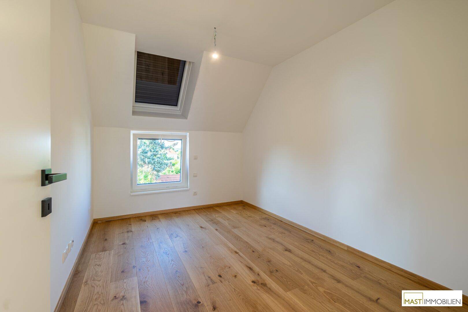 Ruhiges Zimmer mit Holzboden, Dachschräge und einem Fenster, ideal als Schlaf- oder Arbeitszimmer.