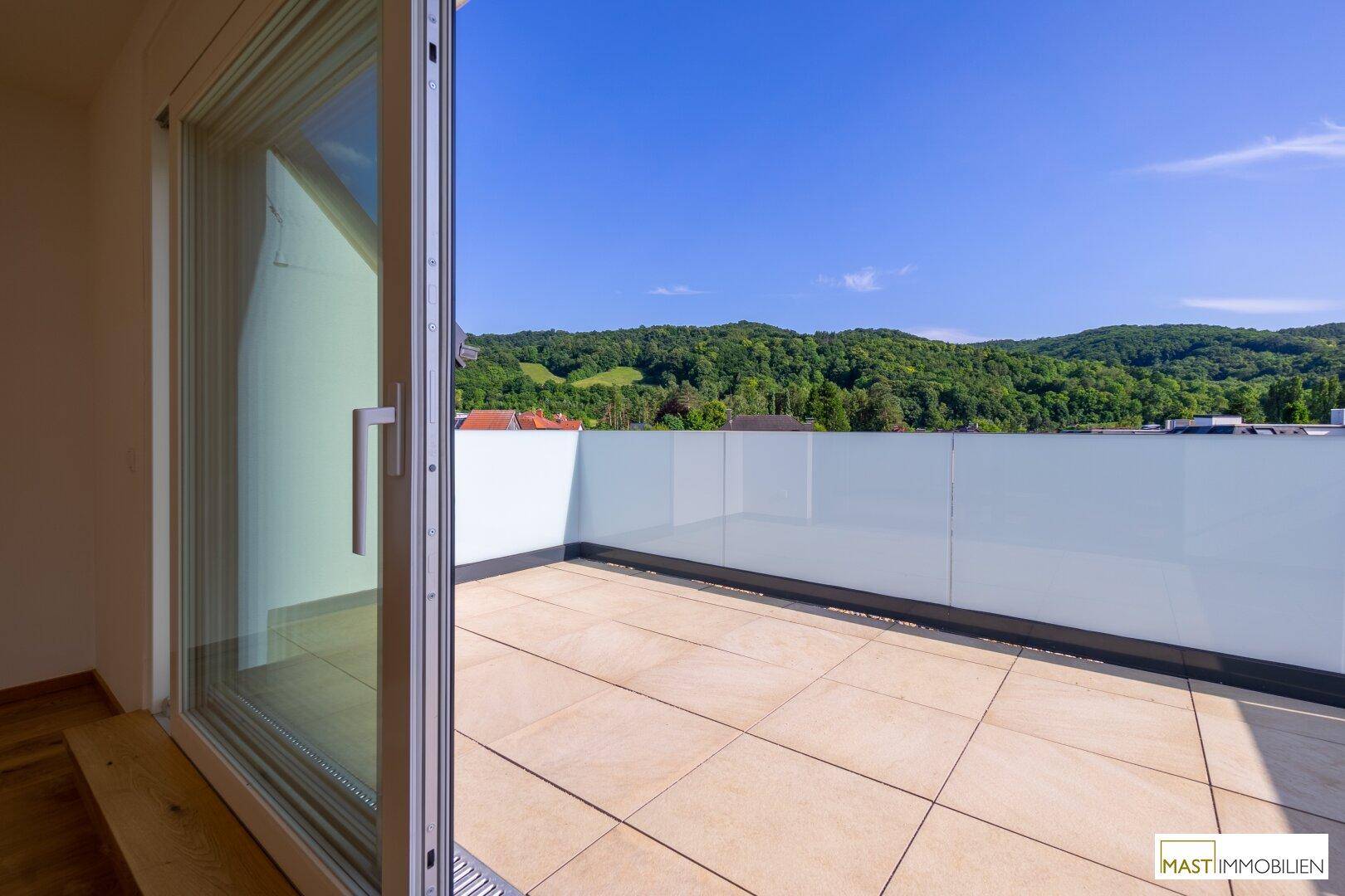 Geräumiger Balkon mit Fliesenboden, Glasbrüstung und weitem Blick auf die grüne Landschaft.