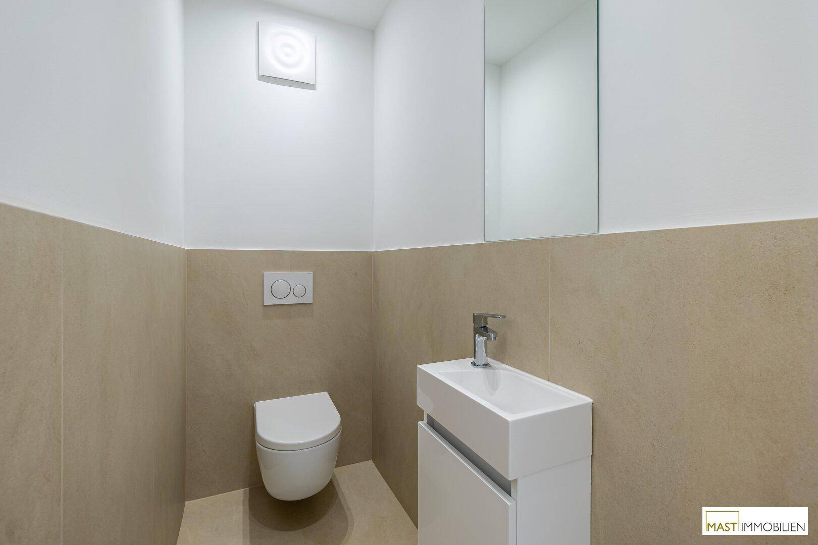 Kleines, modernes Gäste-WC mit Wand-WC, Waschbecken und Spiegel in beigefarbenen Fliesen.