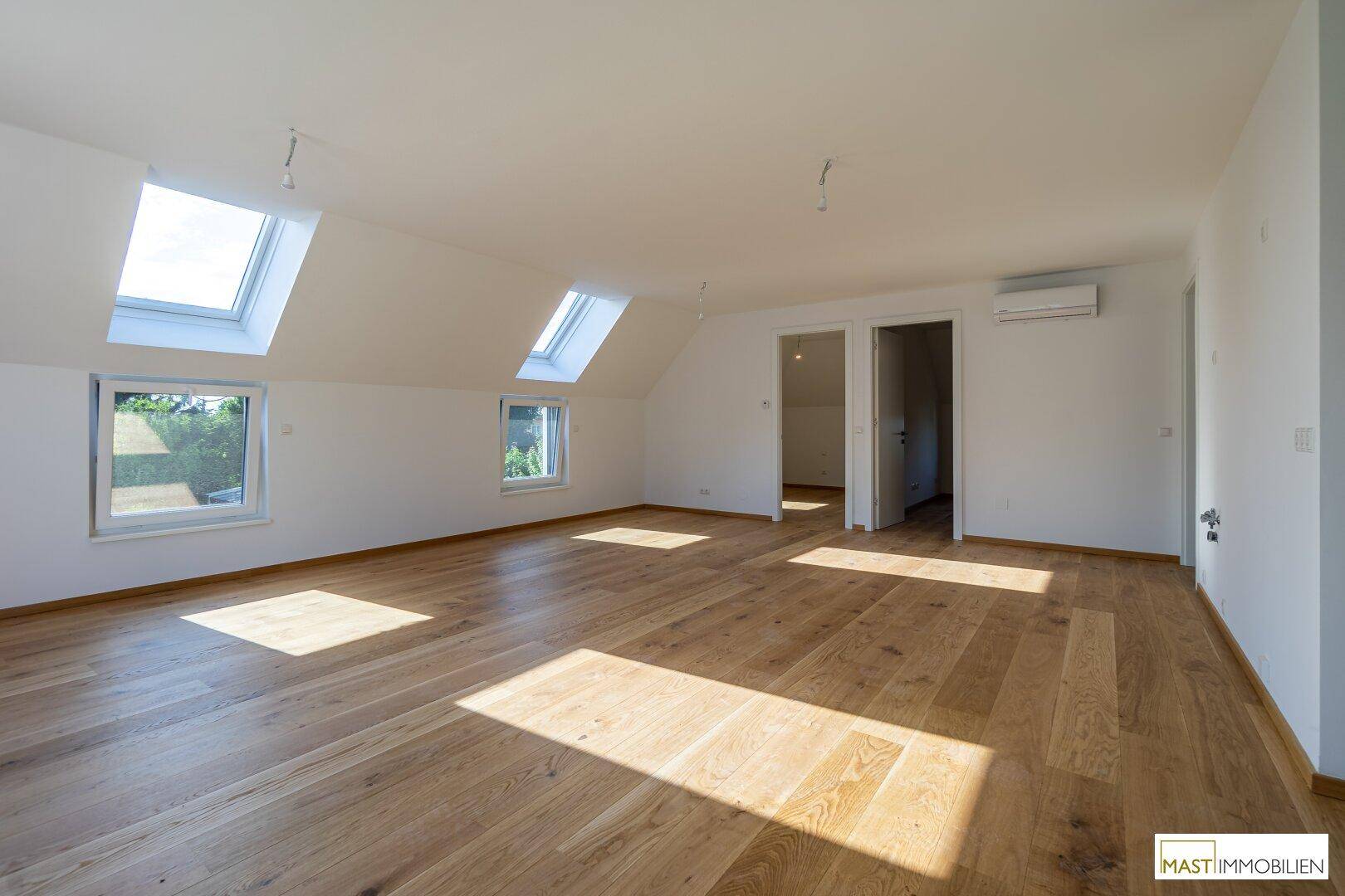 Großes, lichtdurchflutetes Zimmer mit Holzboden, Dachfenstern und Zugang zu weiteren Räumen.