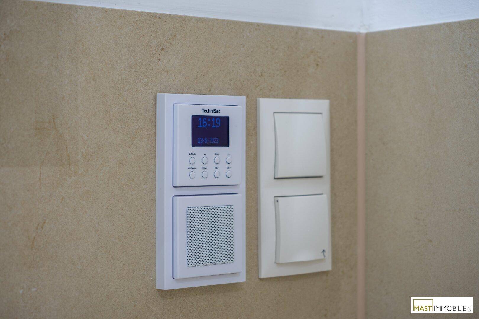 Detailansicht eines modernen Steuerungspanels und Lichtschalters an der gefliesten Wand im Badezimmer.