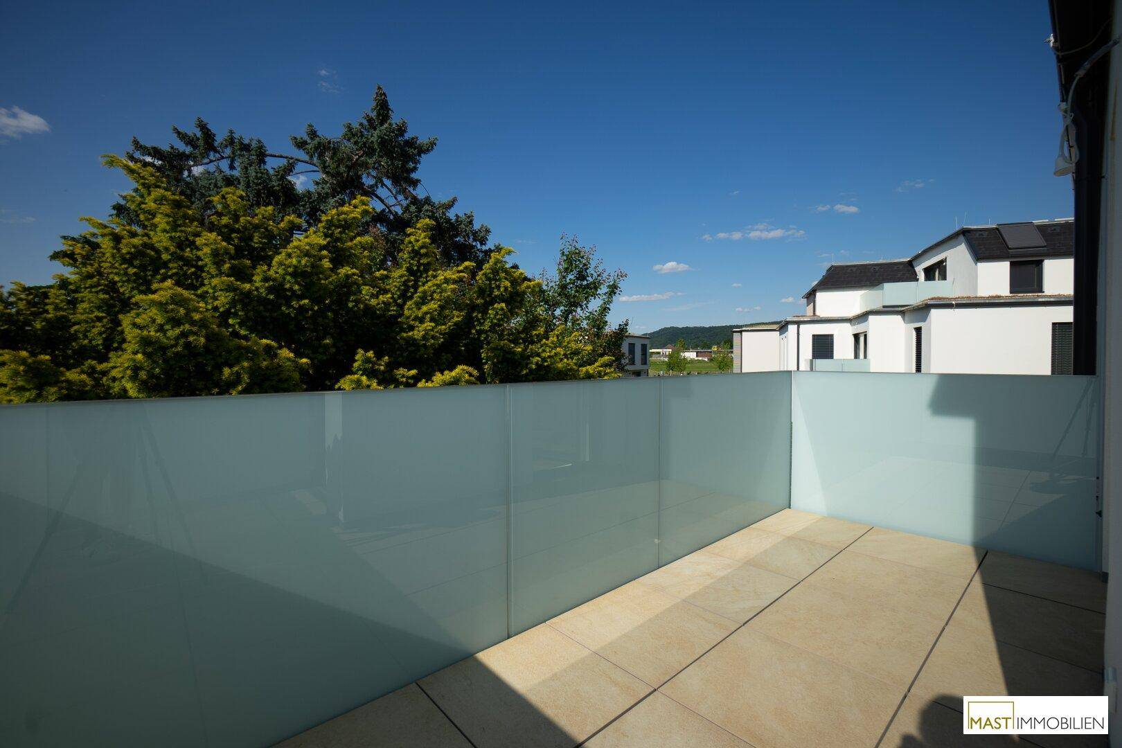 Heller Balkon mit moderner Glasbrüstung und Blick auf die umliegende Wohngegend.