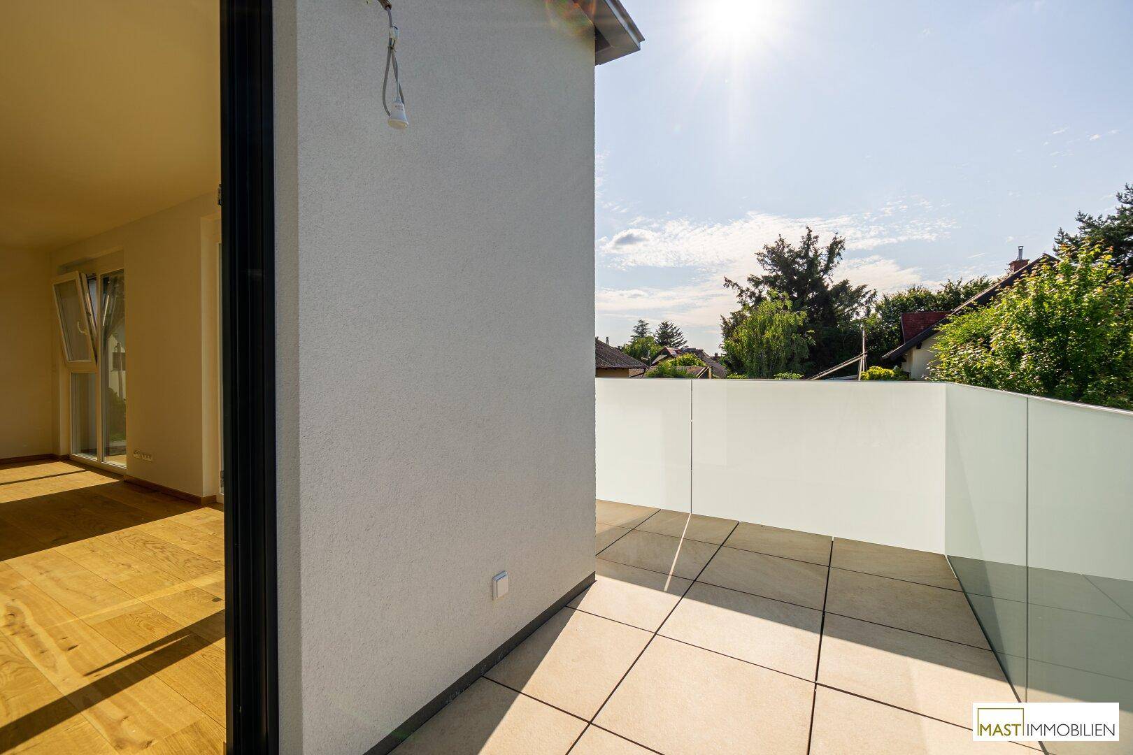 Sonniger Balkon mit Fliesenboden und moderner Glasbrüstung, ideal zum Entspannen im Freien.