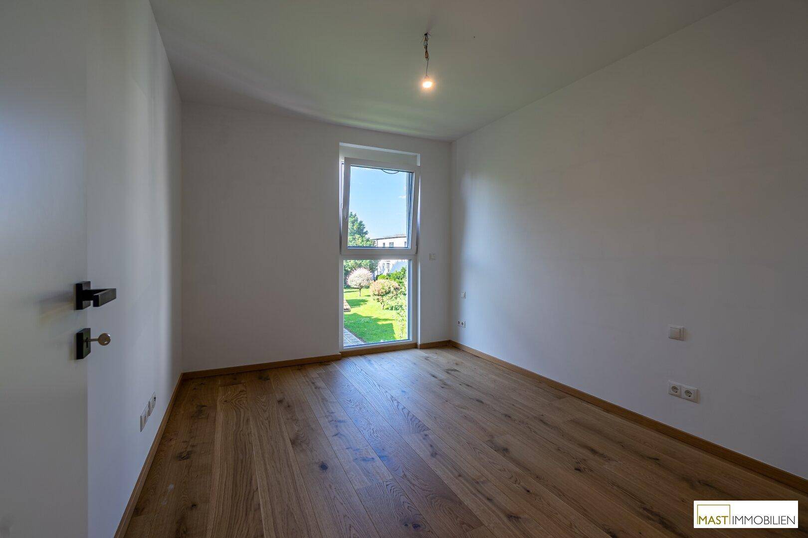 Unmöbliertes Schlafzimmer mit Holzboden und Fenster, das einen Blick auf den Garten bietet.