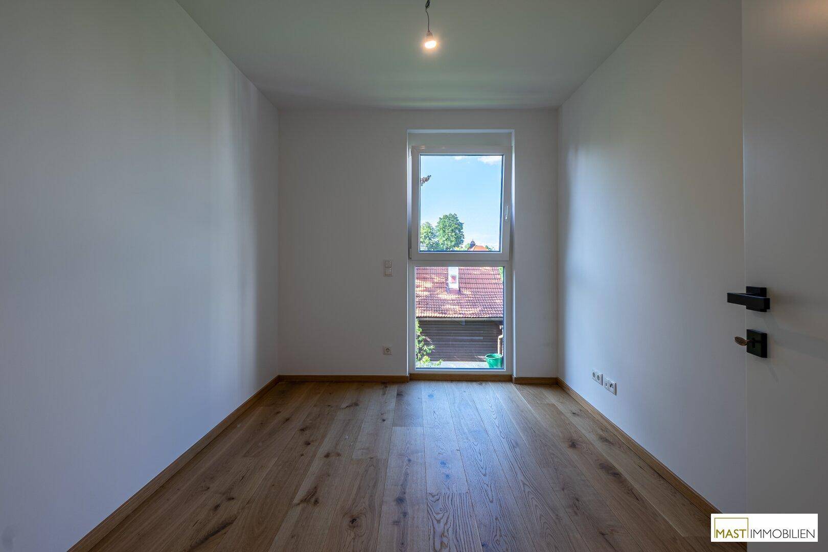 Leeres Schlafzimmer mit Holzboden und einem Fenster, das viel Tageslicht hereinlässt.