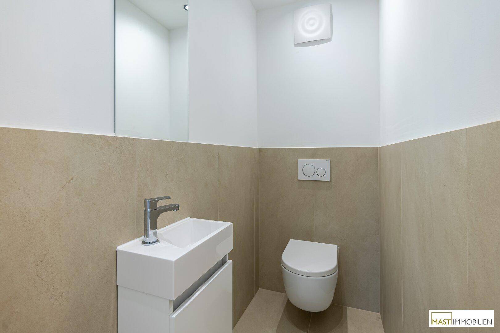 Modernes Gäste-WC mit wandhängender Toilette, kleinem Waschbecken und beigefarbenen Fliesen.