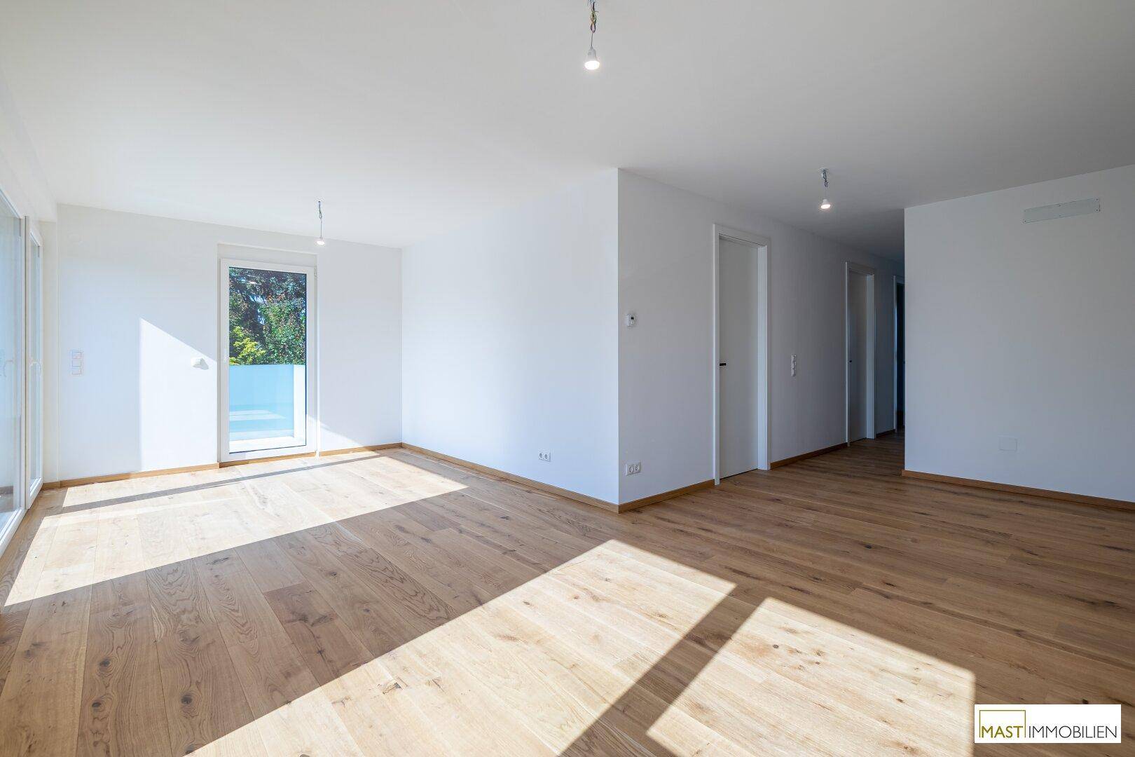 Geräumiges, lichtdurchflutetes Wohnzimmer mit hellem Holzboden und weiß gestrichenen Wänden.