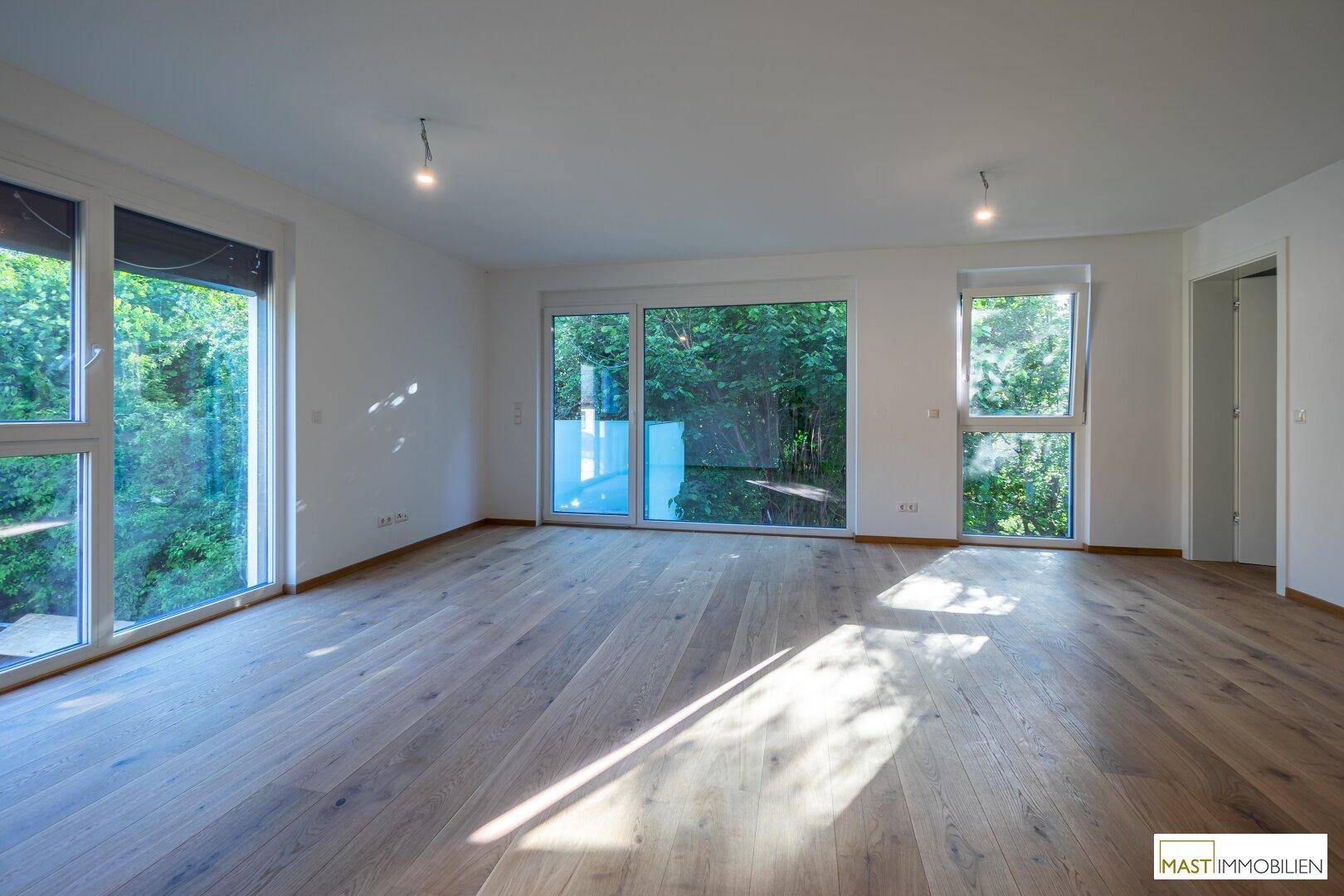 Großzügiges Wohnzimmer mit hellem Holzboden und weitem Blick ins Grüne, ideal für Entspannung.
