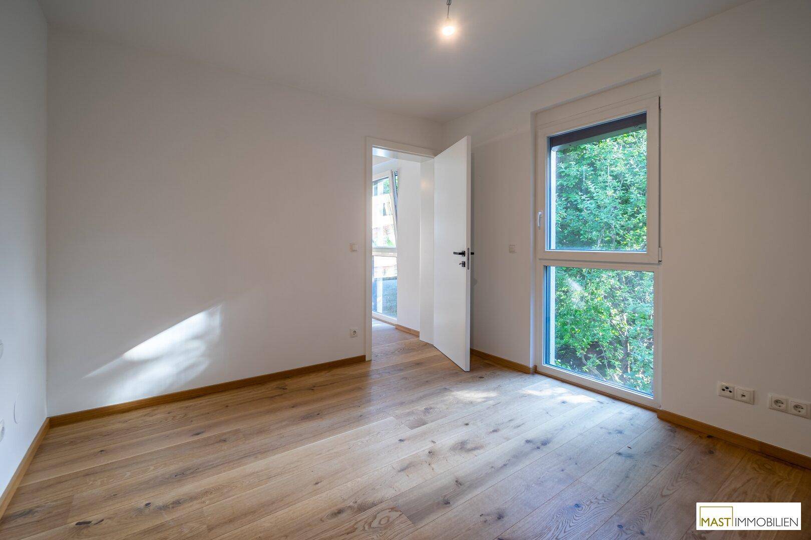 Helles Zimmer mit Holzboden und großem Fenster, ideal als Schlaf- oder Arbeitszimmer nutzbar.