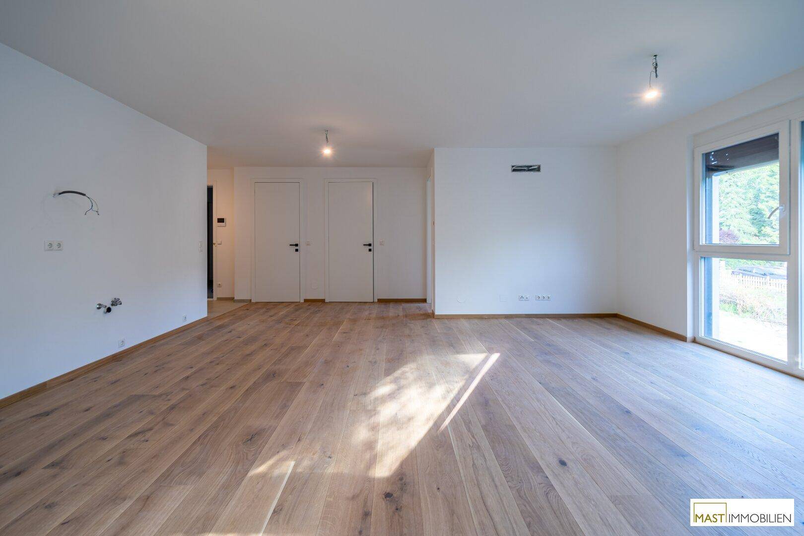 Geräumiges Wohnzimmer mit hellem Holzboden und weißen Wänden, bereit für individuelle Gestaltung.