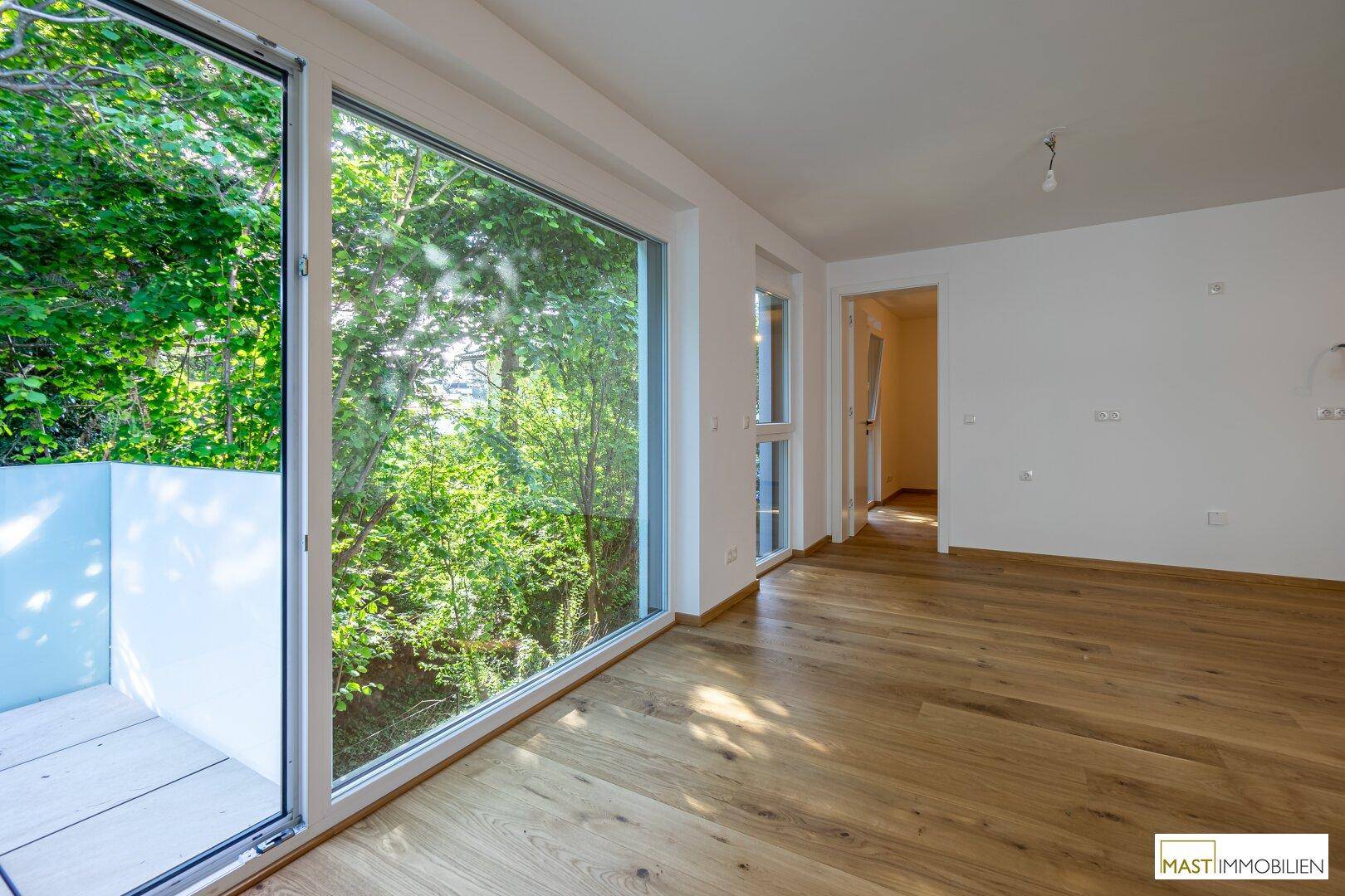 Geräumiges Wohnzimmer mit Eichenparkett und bodentiefen Fenstern mit Blick ins Grüne.