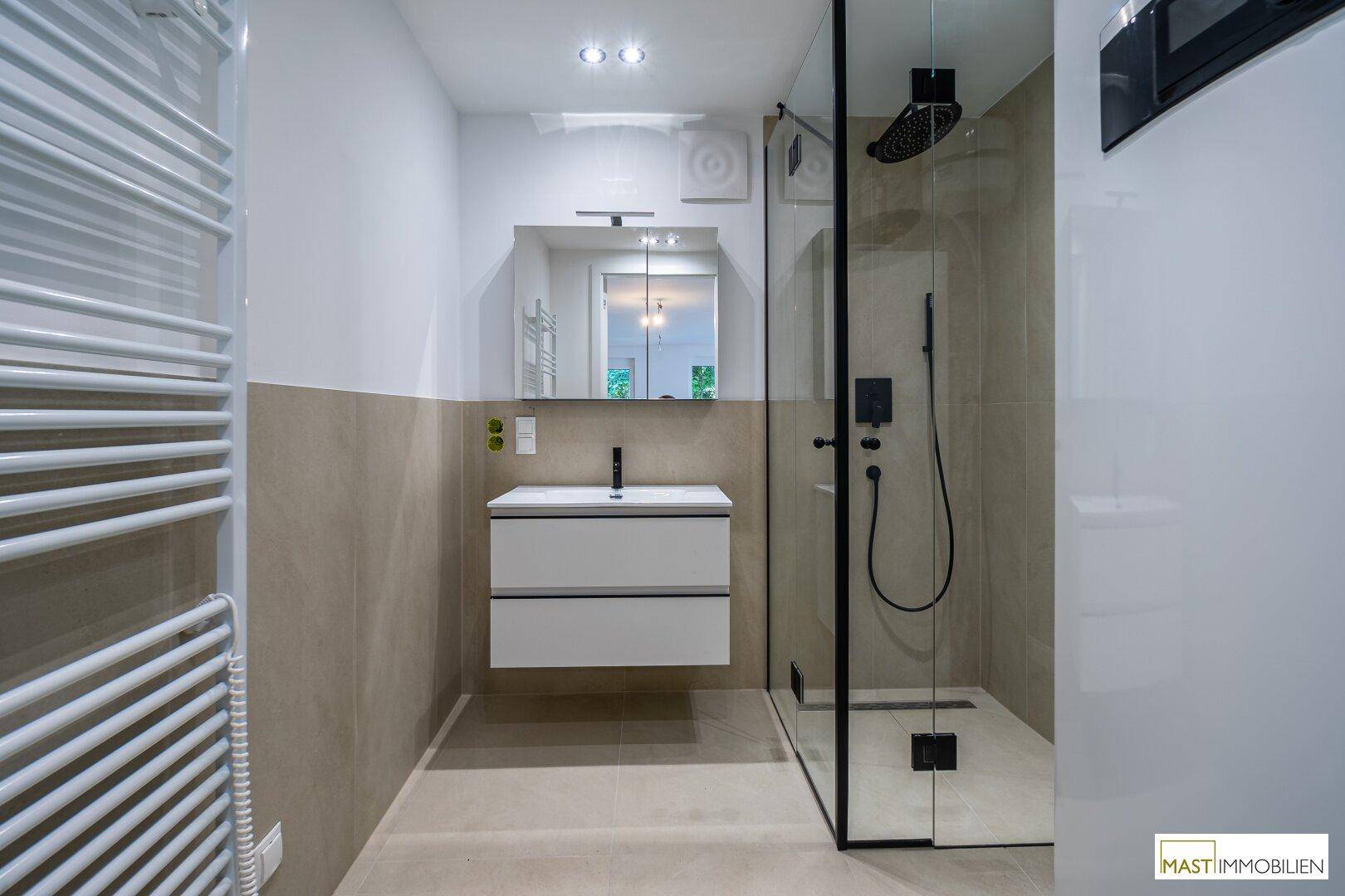 Stilvolles Badezimmer mit großer Duschkabine, Wandspiegel und Handtuchheizkörper.