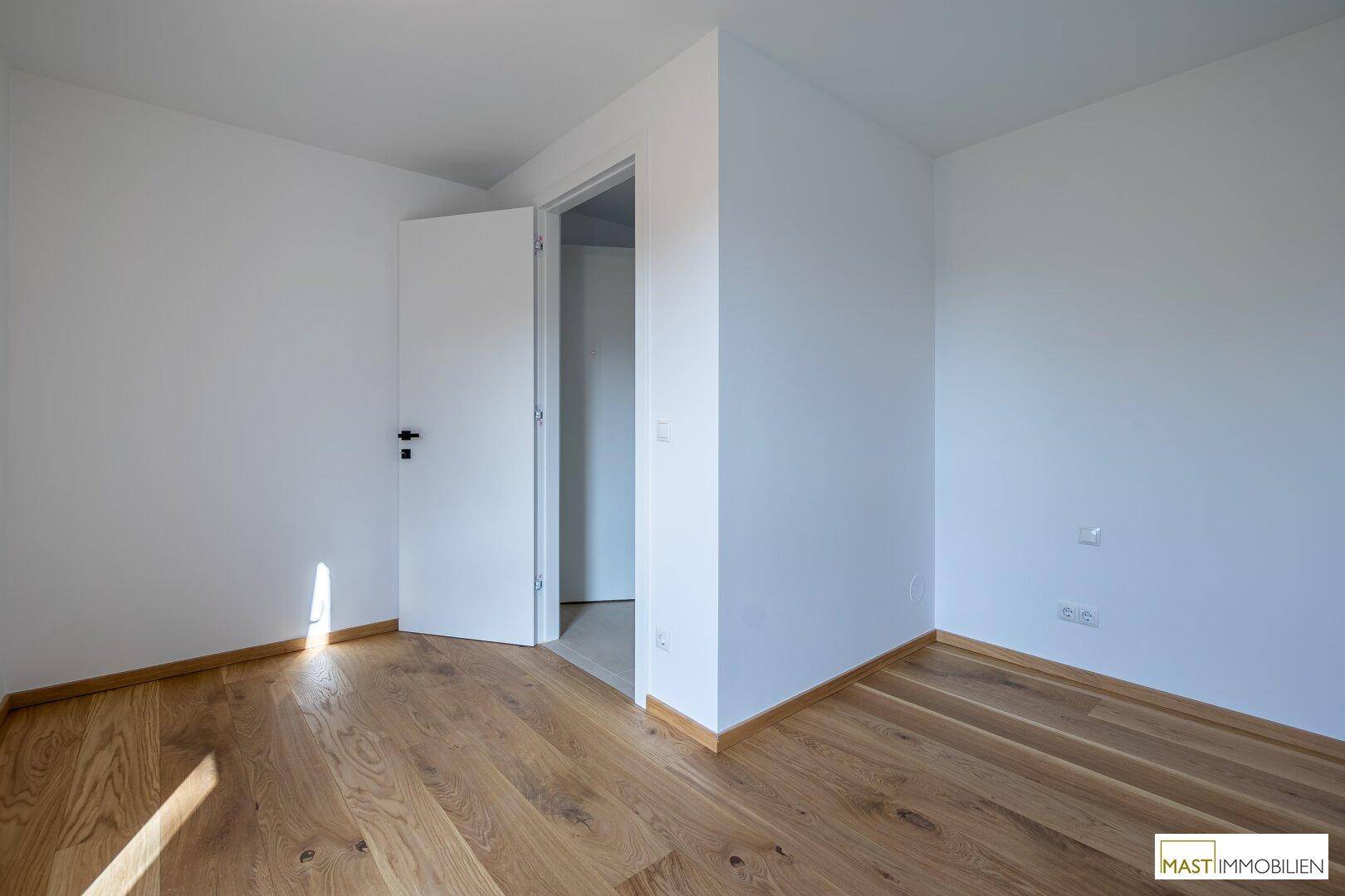Leeres Zimmer mit weiß gestrichenen Wänden und Holzboden, bereit zur individuellen Einrichtung.