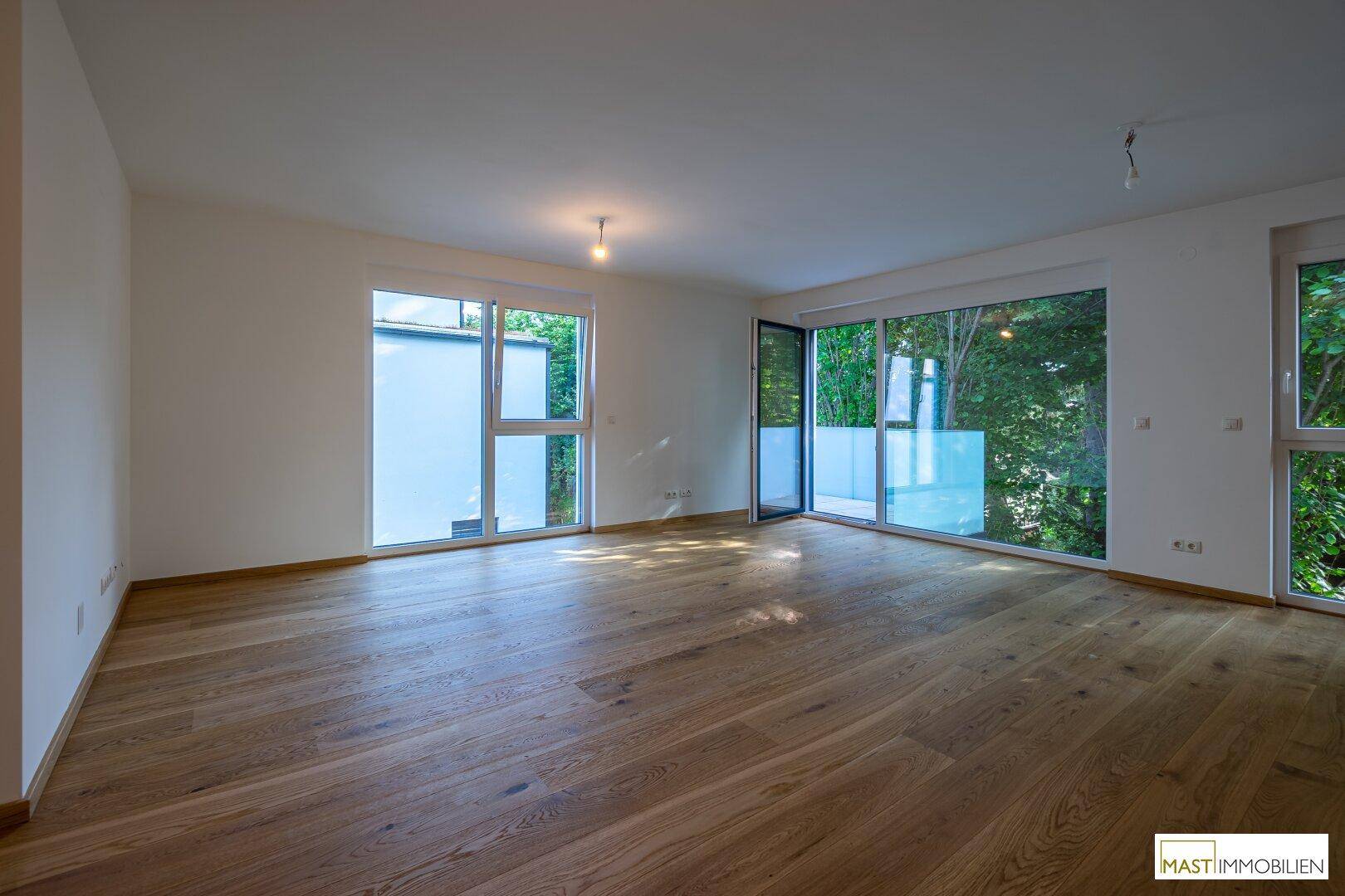 Lichtdurchfluteter Wohnraum mit Holzboden und großen Fenstern, die eine angenehme Atmosphäre schaffen.
