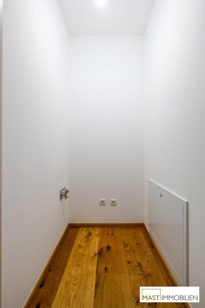 Praktischer Abstellraum mit Holzfußboden und Anschlüssen, ideal für Waschmaschine oder Lagerung.