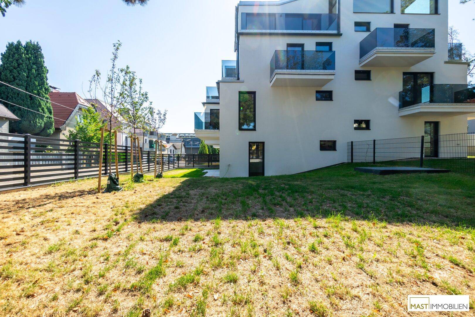 Weitläufiger Gartenbereich mit Rasenfläche und junger Bepflanzung neben dem modernen Wohngebäude.