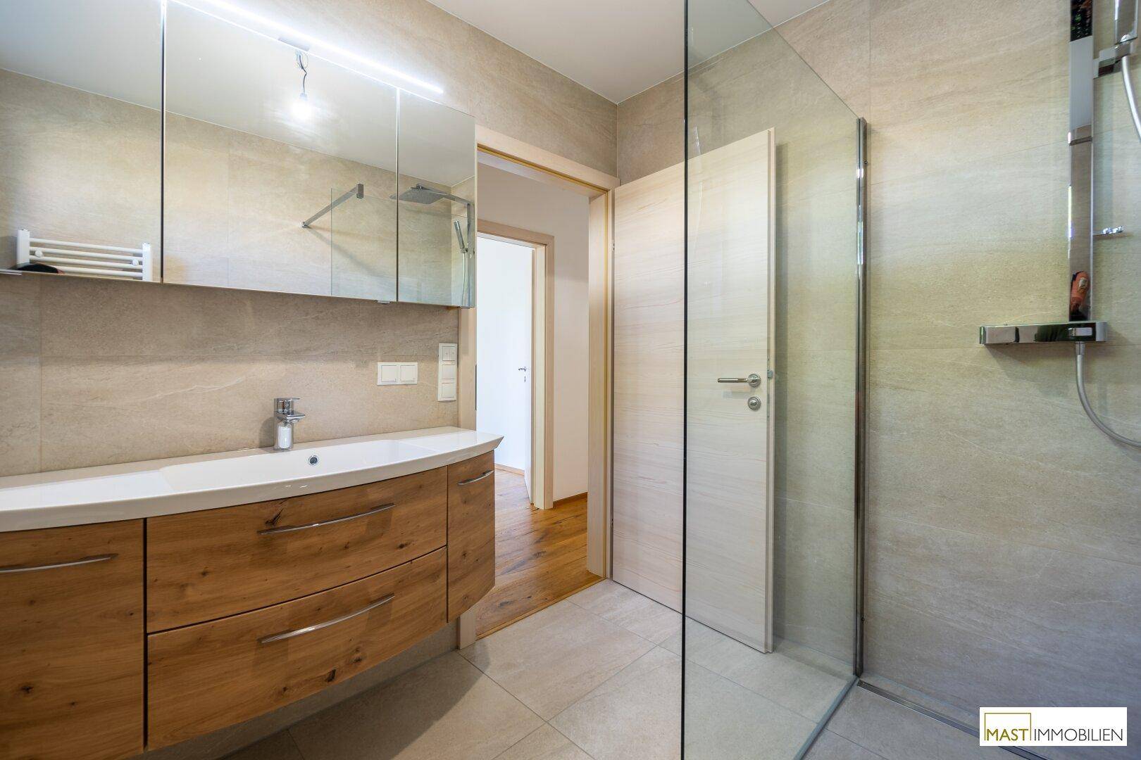 Modernes Badezimmer mit großformatigen Fliesen, Holzwaschtisch und einer geräumigen Glasdusche.