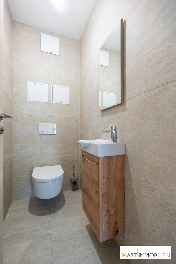 Kleines Gäste-WC mit wandhängender Toilette, modernem Waschbecken und hellen Fliesen.