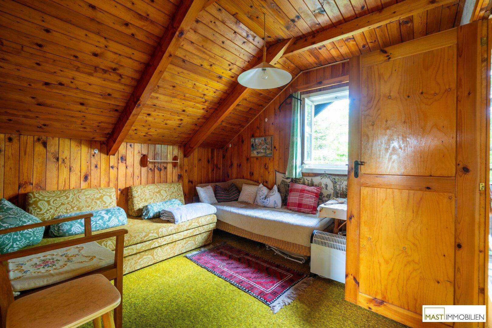 Gemütliches Zimmer im Dachgeschoss mit Holzvertäfelung, Schlafsofas und schrägen Decken.