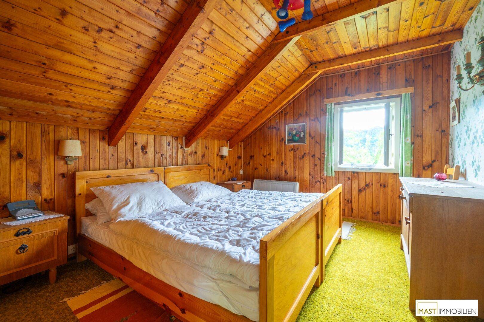 Schlafzimmer im Dachgeschoss mit Holzvertäfelung, schrägen Decken und traditionellem Doppelbett.