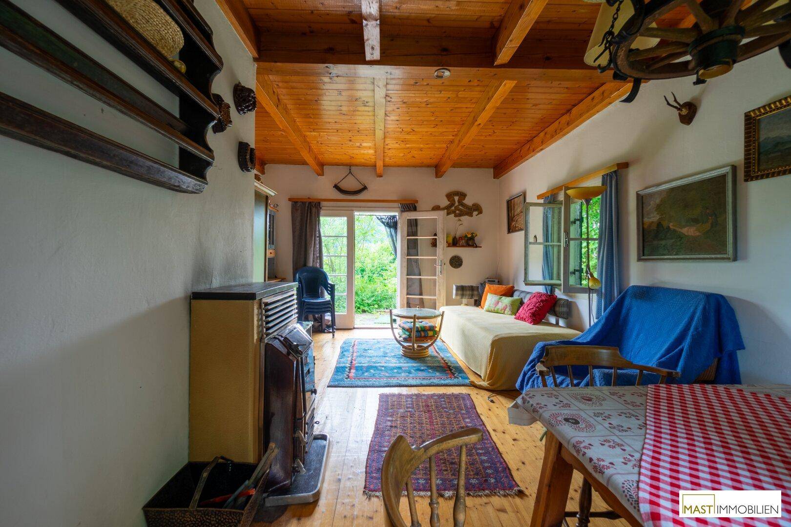 Gemütliches Wohnzimmer im alpinen Stil mit Holzbalkendecke, Kaminofen und Zugang zum Garten.