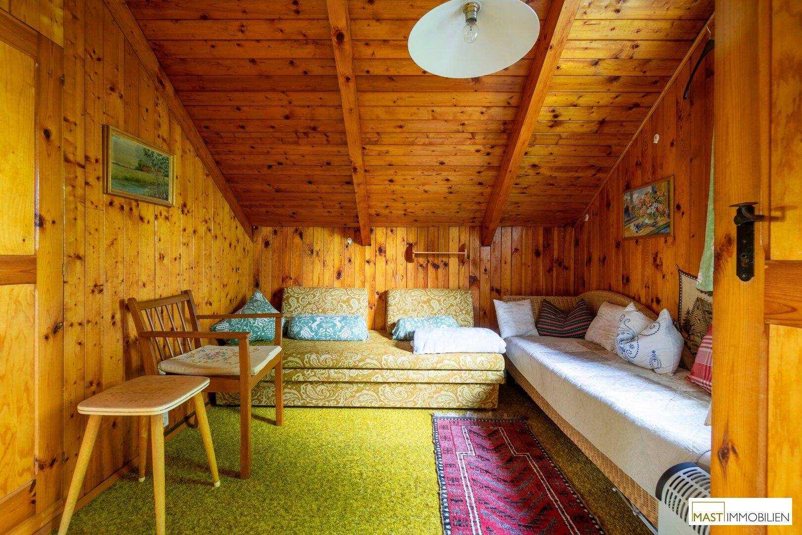 Rustikales Zimmer mit Holzvertäfelung, Teppichboden und traditionellen Möbeln im Dachgeschoss.