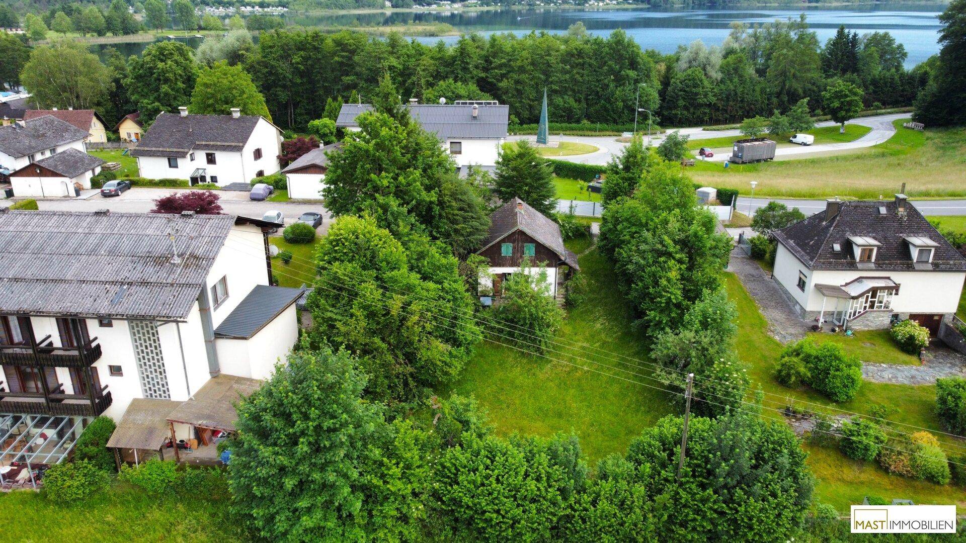 Weitläufige Luftaufnahme des Anwesens mit See im Hintergrund und umliegender Bebauung.