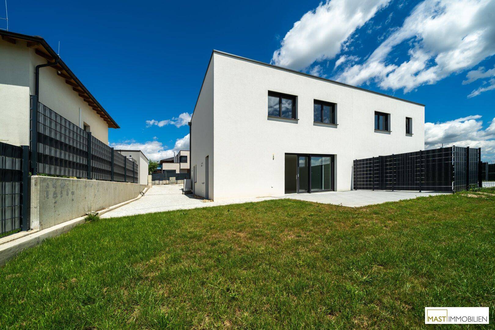 Modernes Reihenhaus mit weißer Fassade, Garten und Terrasse unter blauem Himmel.