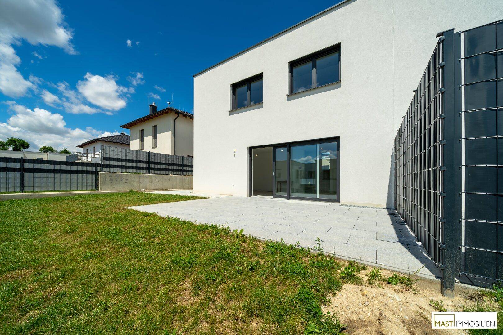 Rückseite des modernen Reihenhauses mit Garten, Terrasse und Blick auf die Umgebung.