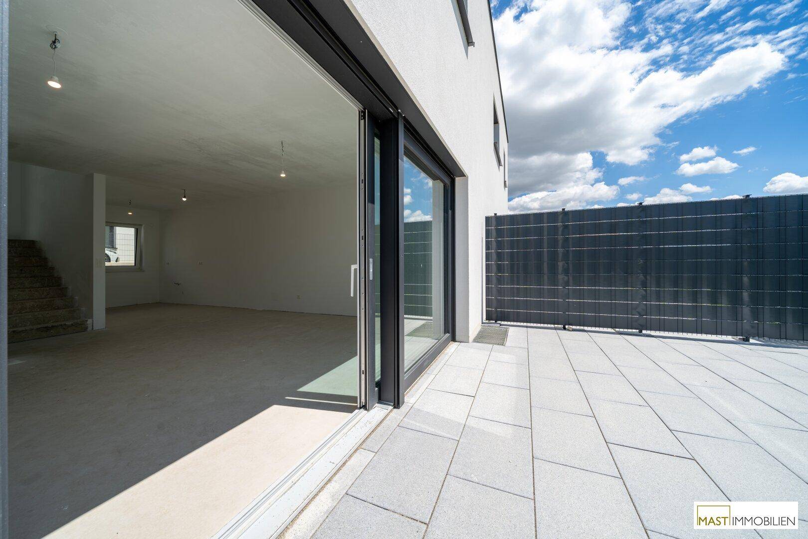 Helle Terrasse mit großen Schiebetüren, die in den noch unfertigen Innenbereich führen.