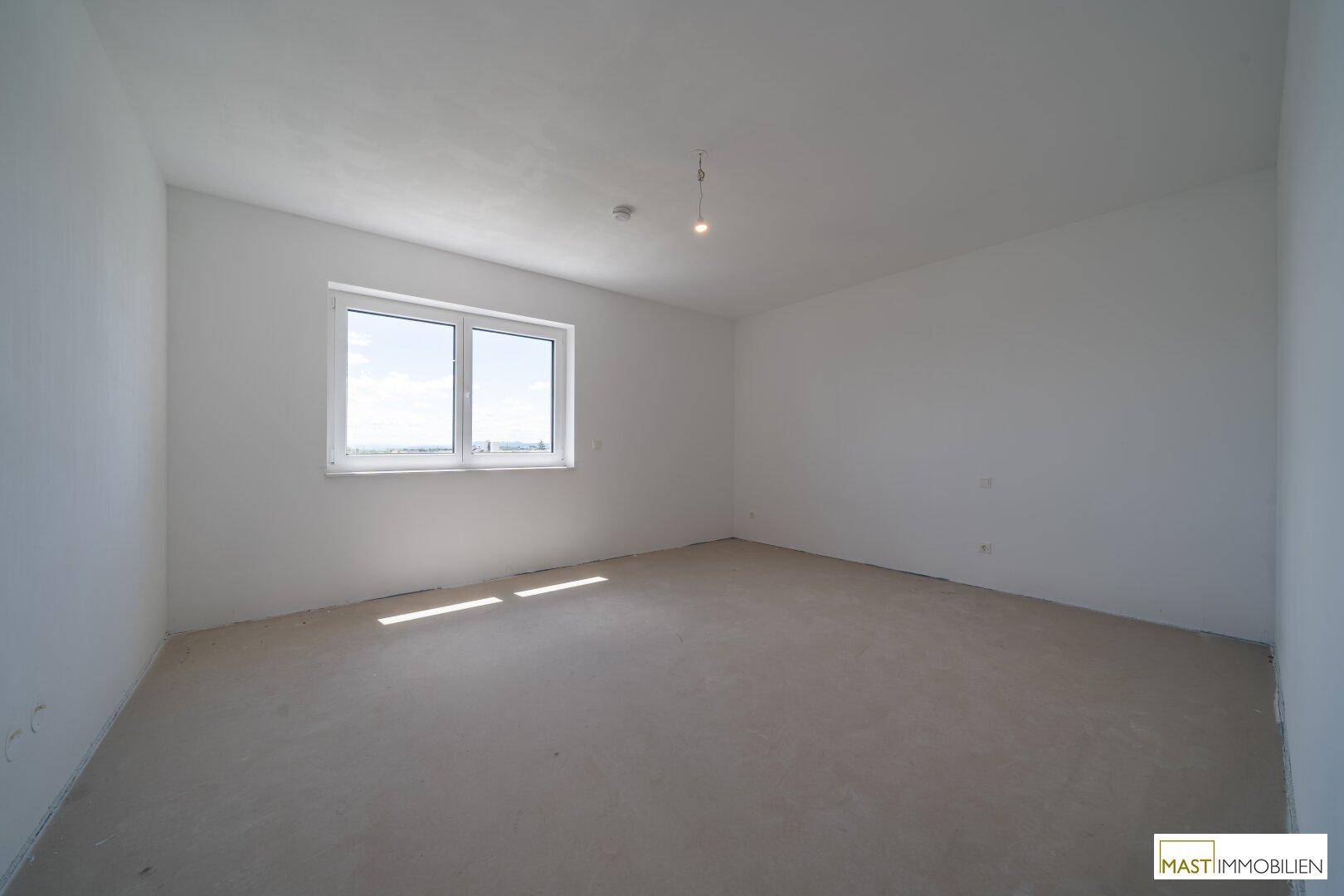 Helles Schlafzimmer im Rohbauzustand mit großem Fenster und Blick ins Grüne.