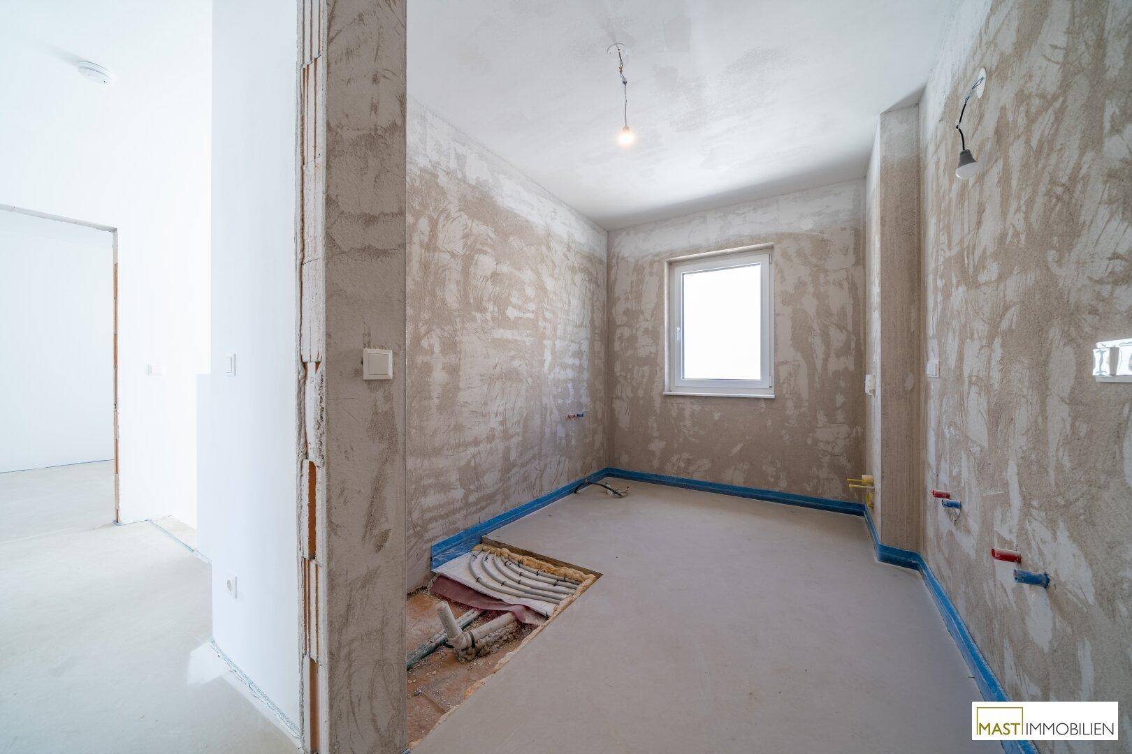 Badezimmer im Rohbau mit sichtbaren Leitungen und einem Fenster für gute Belüftung.