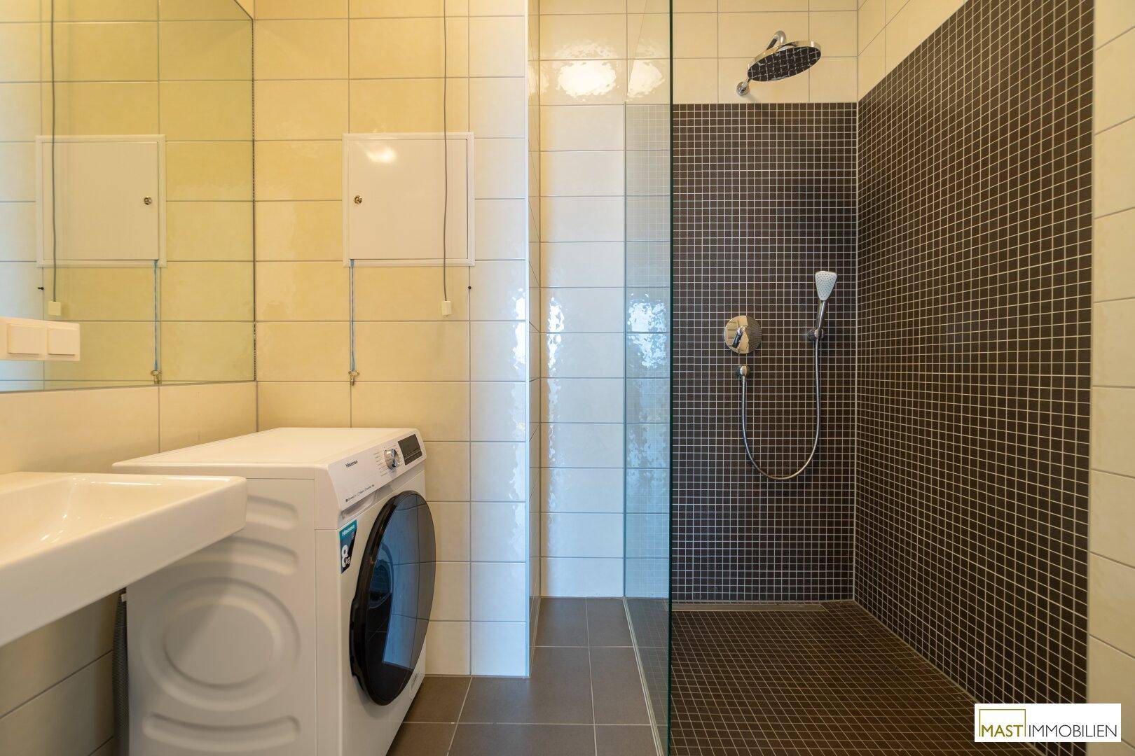 Modernes Badezimmer mit ebenerdiger Dusche, Waschmaschine und großem Spiegel über dem Waschbecken.