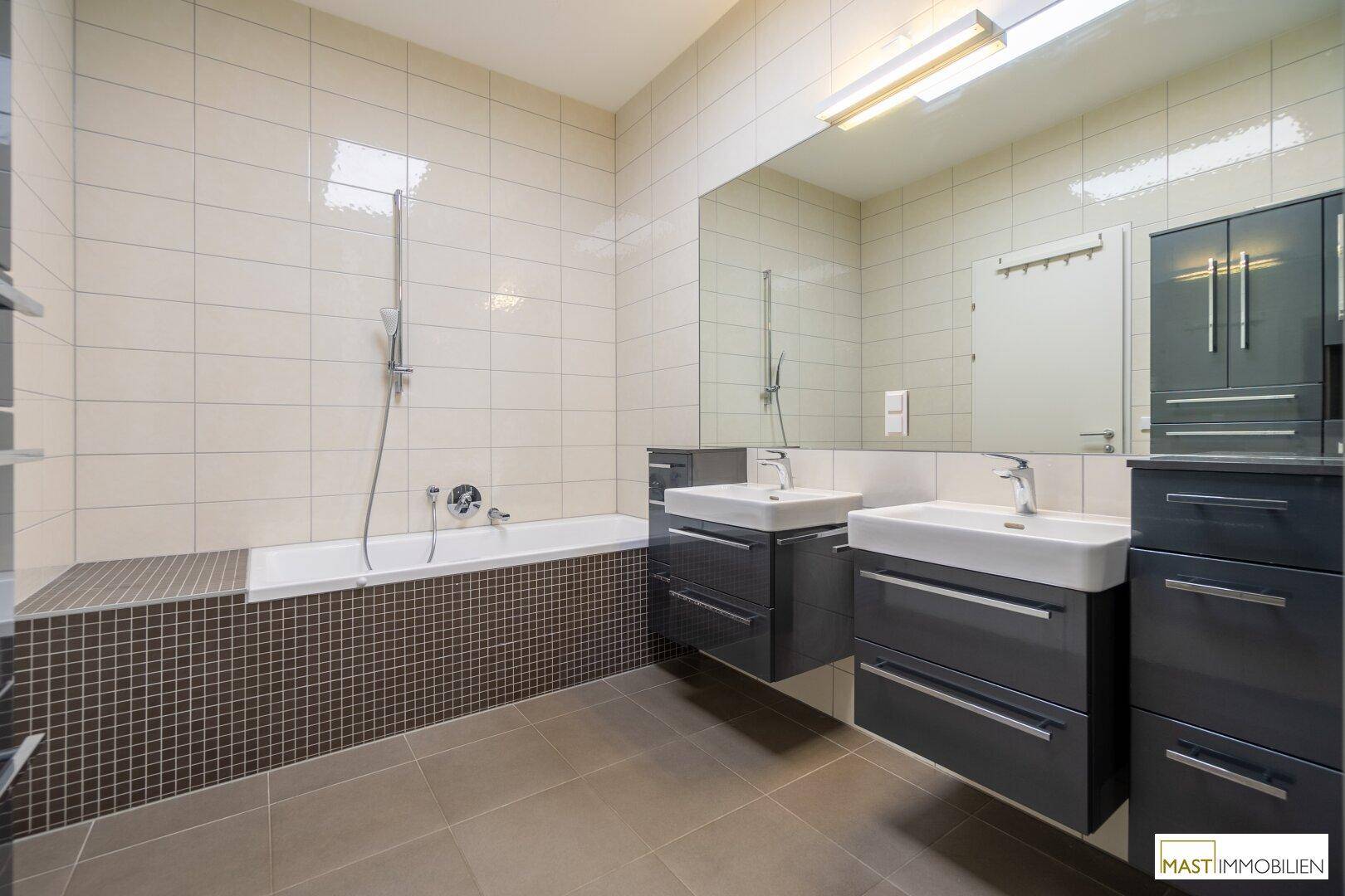 Modernes Badezimmer mit Doppelwaschbecken und einer integrierten Badewanne, gefliest in Grau und Weiß.