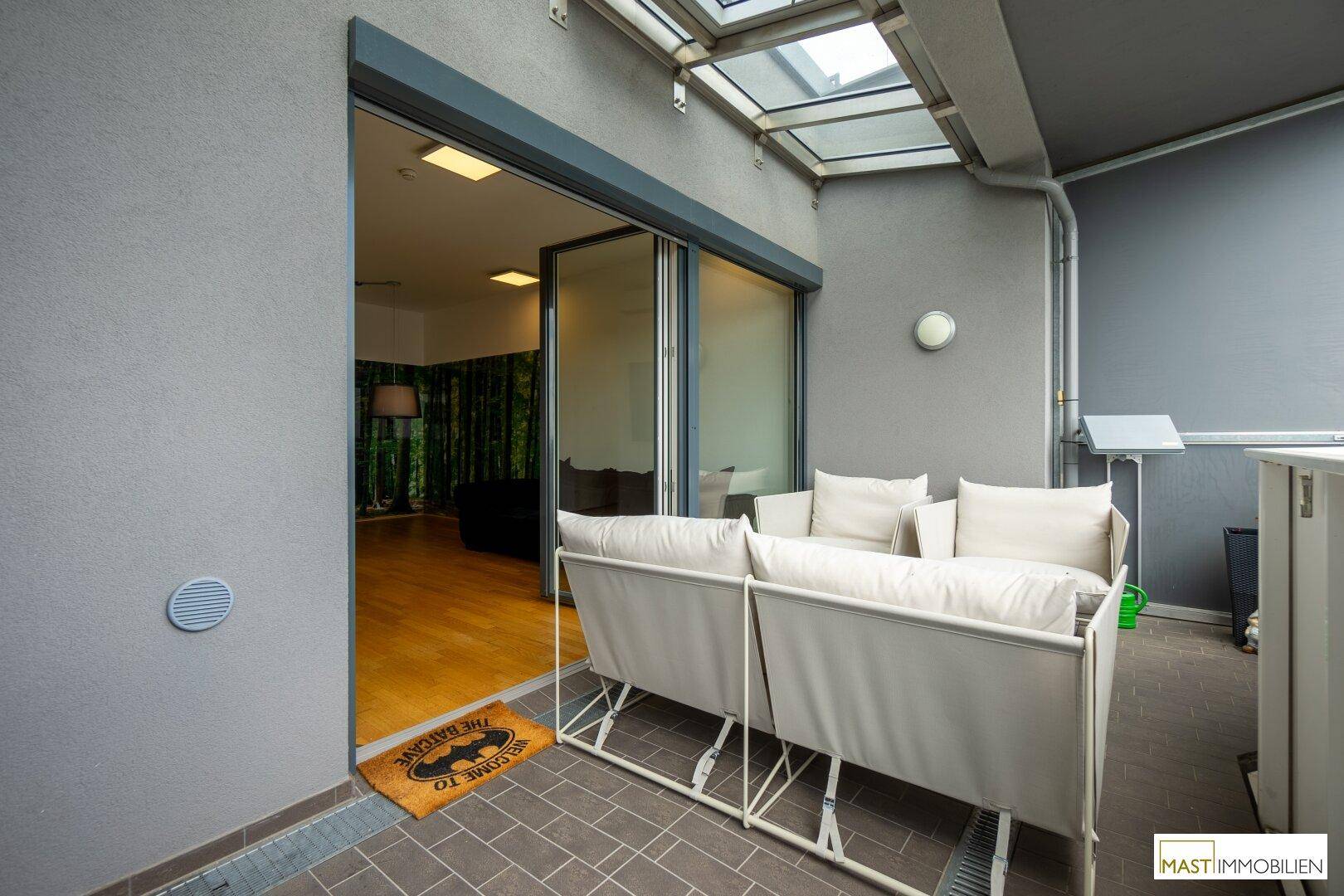 Möblierter Balkon mit Blick durch die großen Schiebetüren in den hellen Wohnbereich der Wohnung.