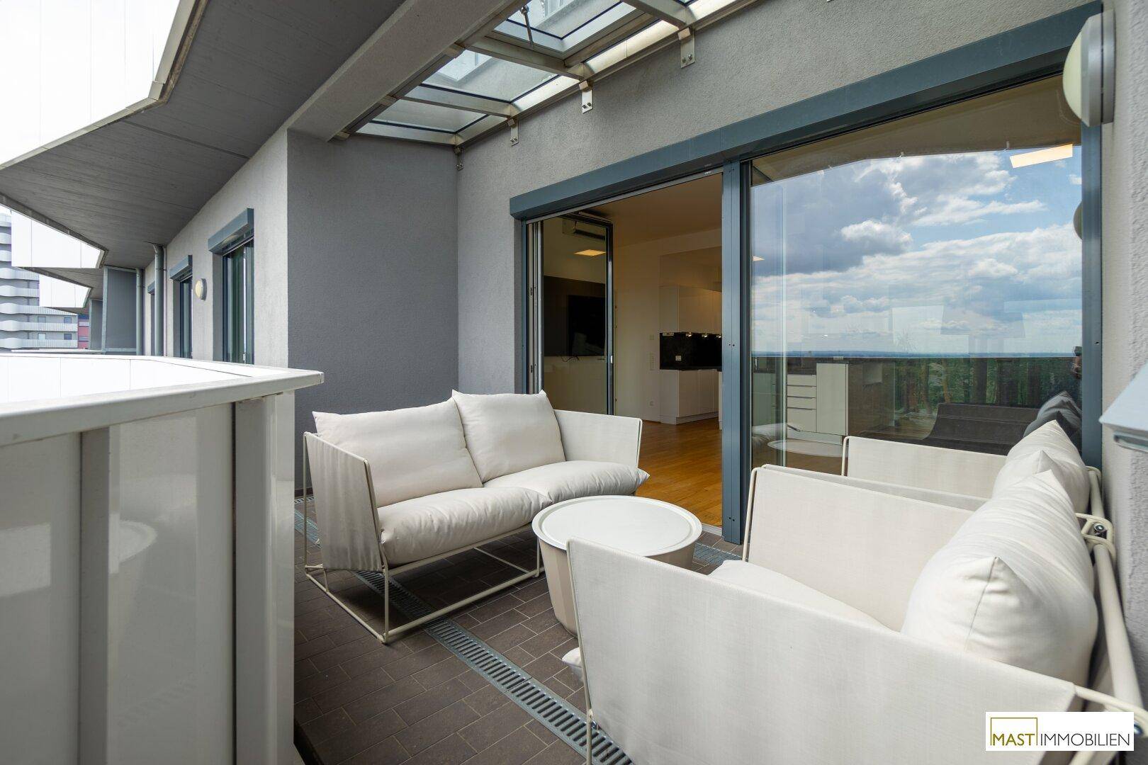 Möblierter Balkon mit bequemen Sitzgelegenheiten und großen Schiebetüren zum hellen Innenbereich.