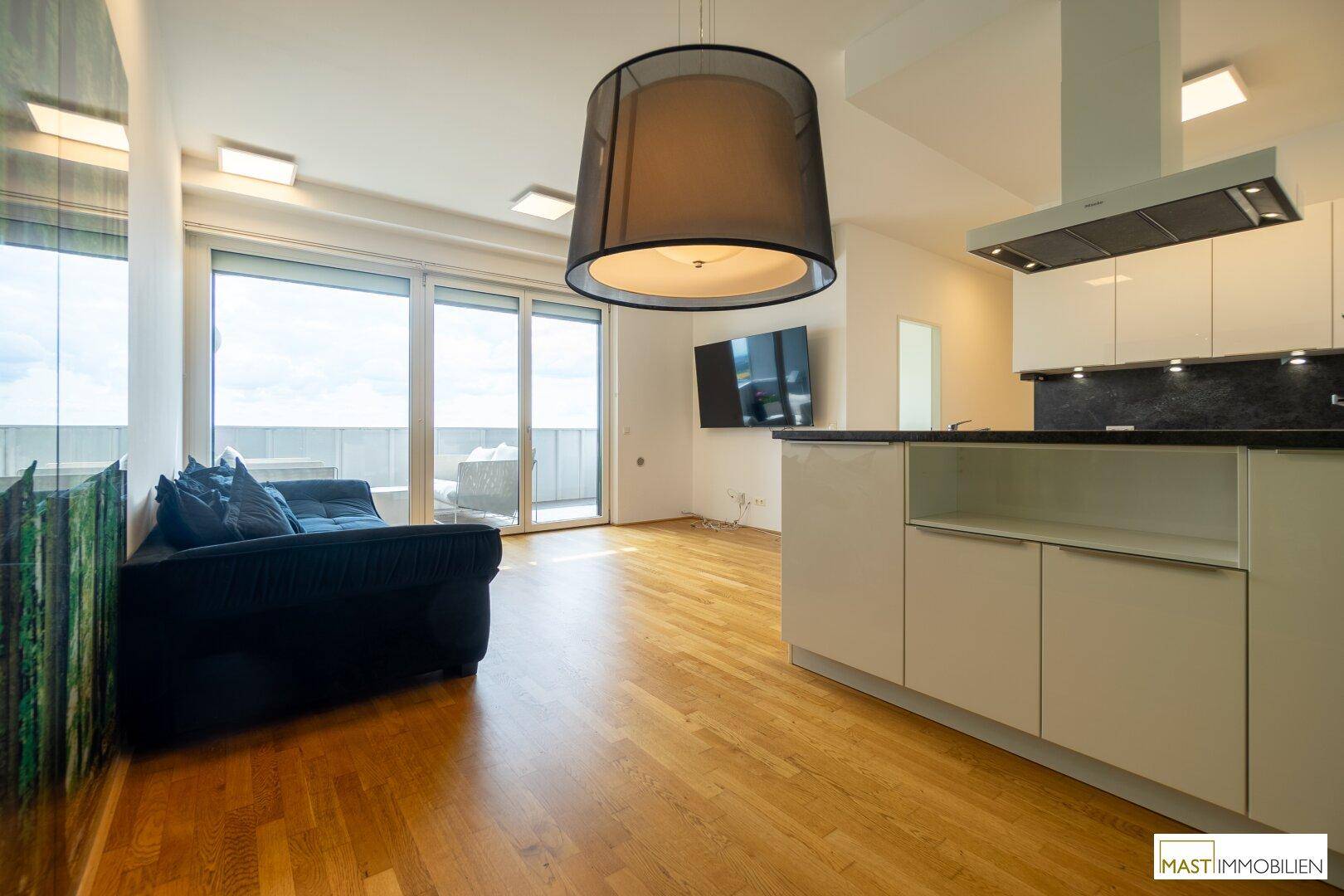Offener Wohnbereich mit moderner Küche, Holzboden und Zugang zu einem Balkon mit weitem Ausblick.