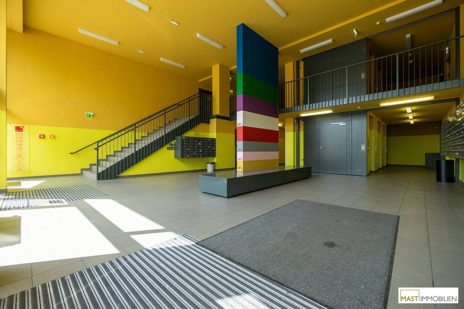 Heller und farbenfroher Eingangsbereich mit Treppe, Briefkästen und Sitzgelegenheiten im Erdgeschoss.