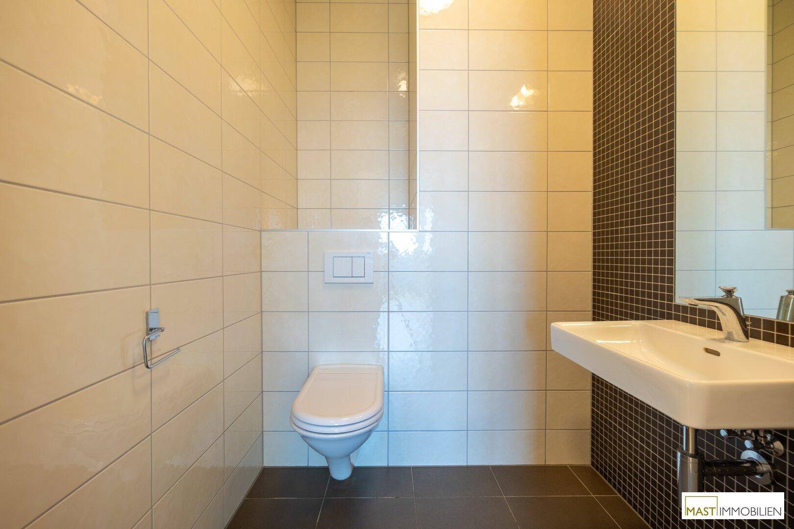 Modernes Gäste-WC mit Wand-WC, Waschbecken und hellen Fliesen in Beige und Braun.