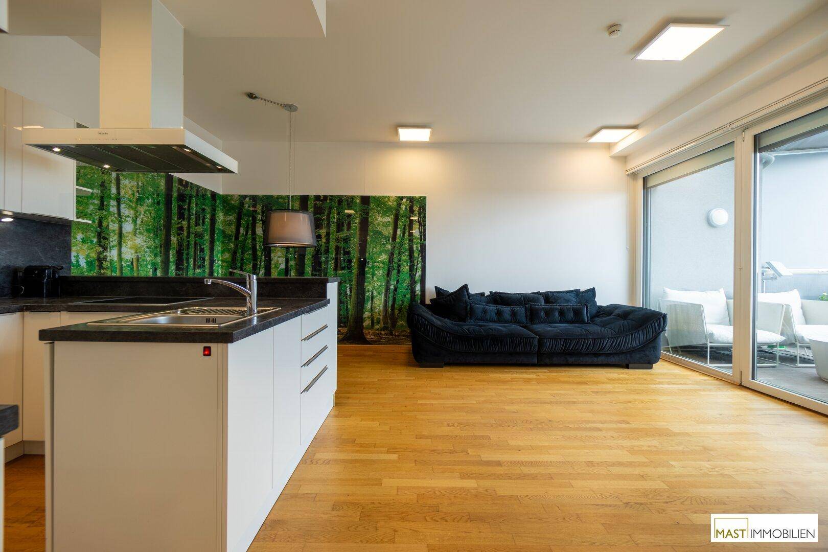 Heller Wohnbereich mit bequemer Couch, Holzboden und großen Schiebetüren zum möblierten Balkon.