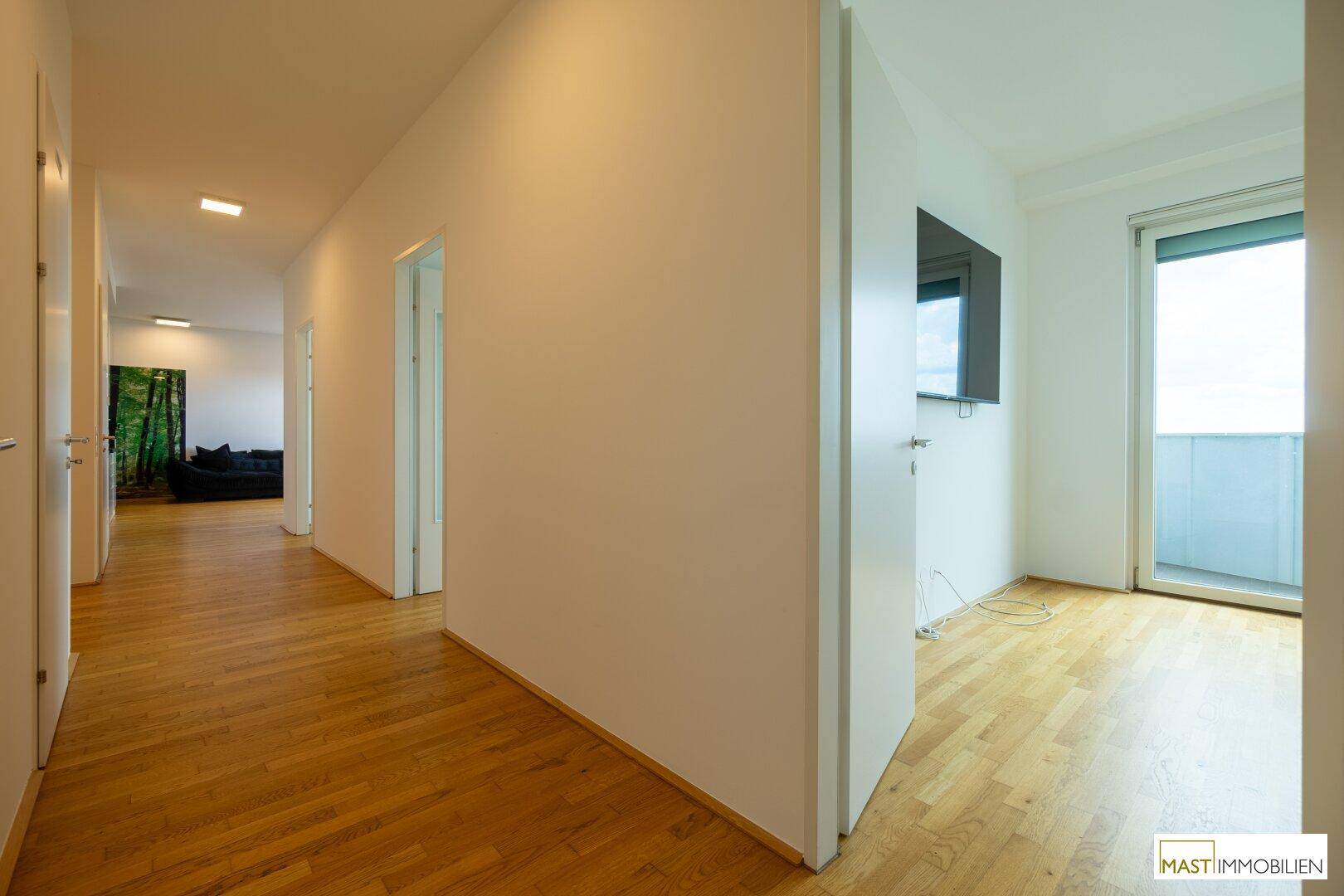 Heller Flur mit Holzboden, der zu verschiedenen Räumen führt, mit Blick auf den Wohnbereich.