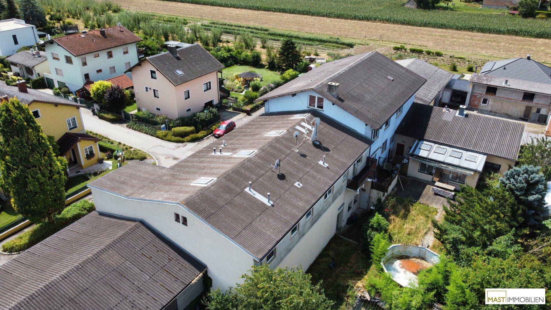 Rückansicht des Gebäudekomplexes von oben, umgeben von Gärten und landwirtschaftlichen Flächen.