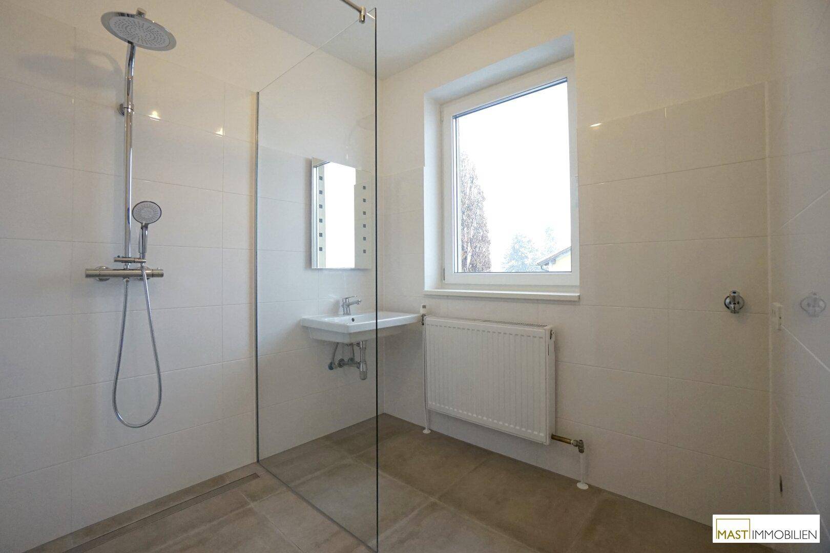 Modernes Badezimmer mit ebenerdiger Dusche, Waschbecken und einem Fenster, das für Tageslicht sorgt.