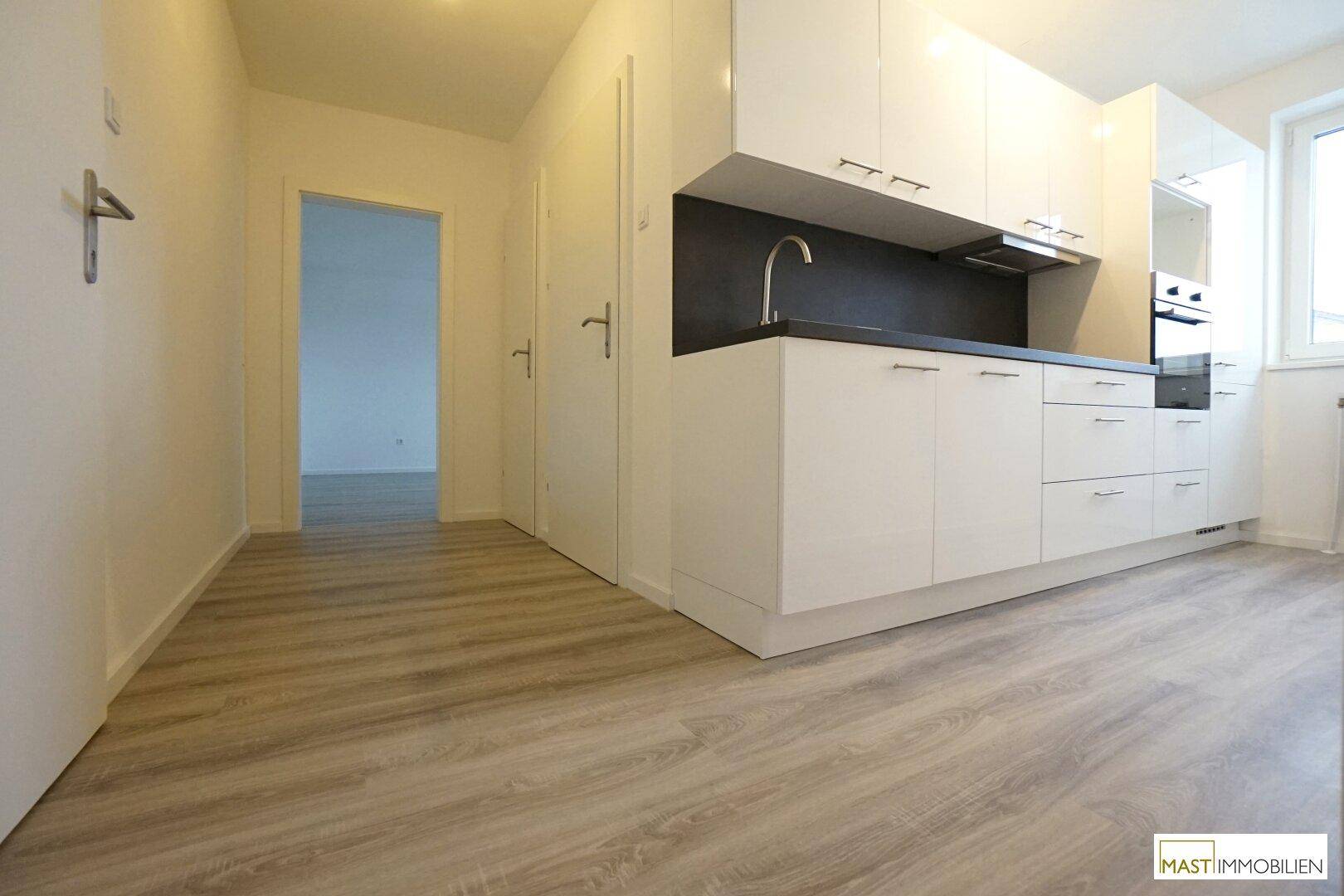 Moderne, weiße Küchenzeile mit integrierten Geräten und dunkler Arbeitsplatte in einem offenen Bereich.