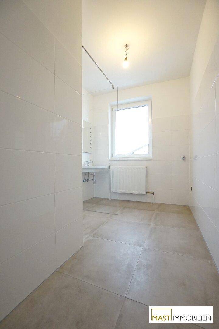 Geräumiges, modernes Badezimmer mit großen Fliesen, ebenerdiger Dusche und einem Fenster.
