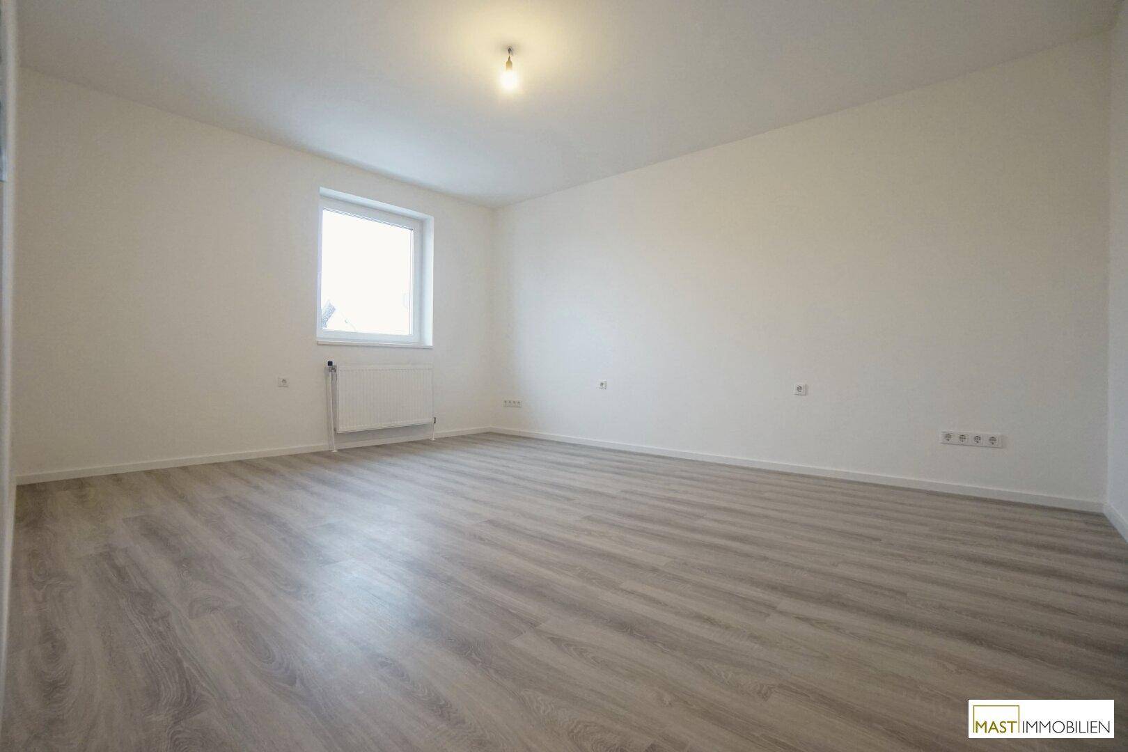 Heller Raum mit Laminatboden, weißen Wänden und einem Fenster, das viel Tageslicht hereinlässt.